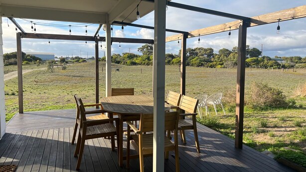 A covered outdoor area with a wooden table and chairs, a pergola with string lights, and a view of a grassy field. - Ramblers Croft- WiFi, Pet friendly outside (Robe)