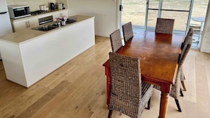 A modern kitchen with a central island, dining table with wicker chairs, and a sliding glass door leading to an outdoor area. - Ramblers Croft- WiFi, Pet friendly outside (Robe)