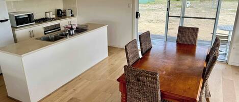 A modern kitchen with a central island, dining table with wicker chairs, and a sliding glass door leading to an outdoor area.