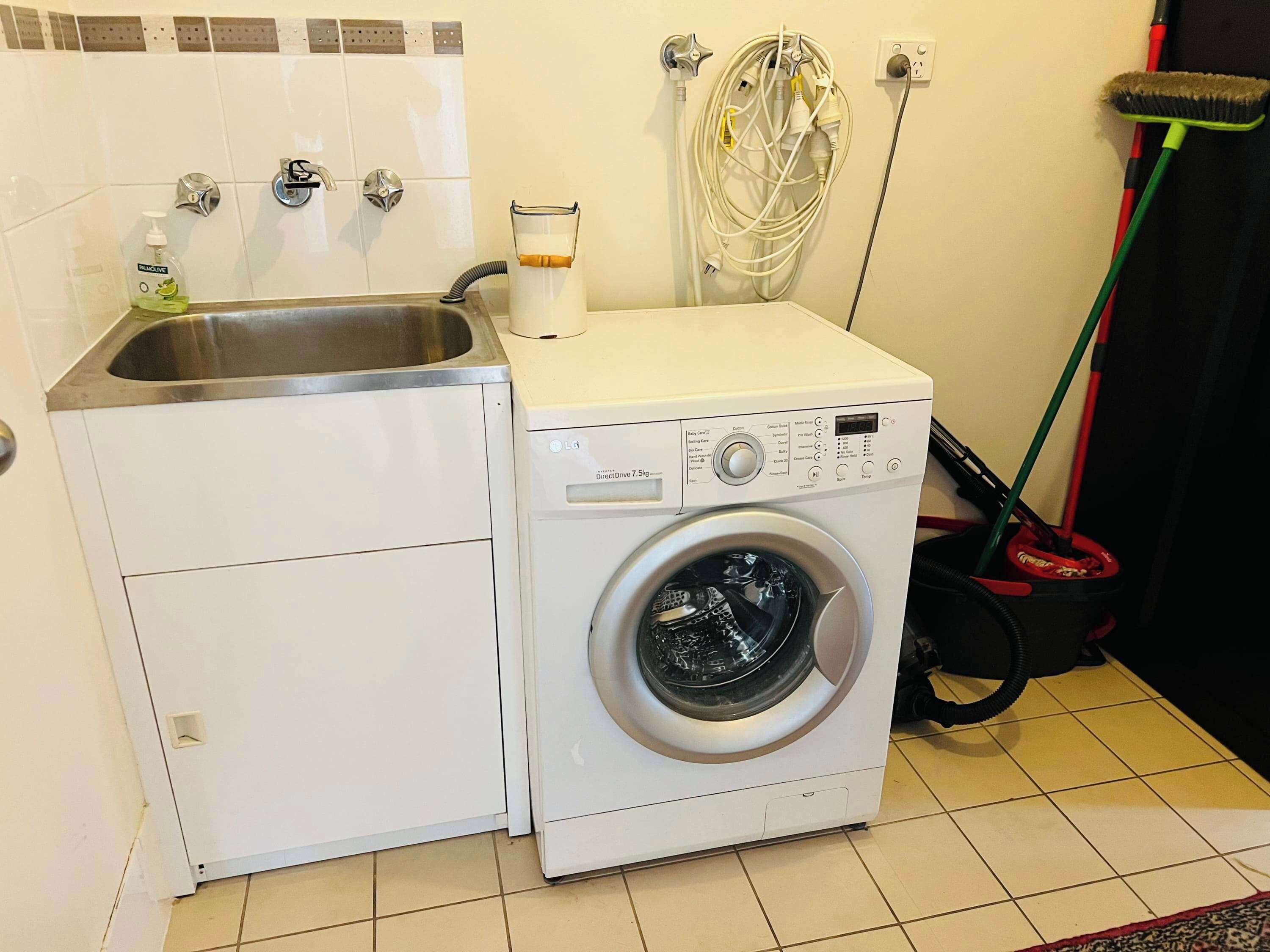 A compact laundry area with a washing machine, a sink, and a hose.