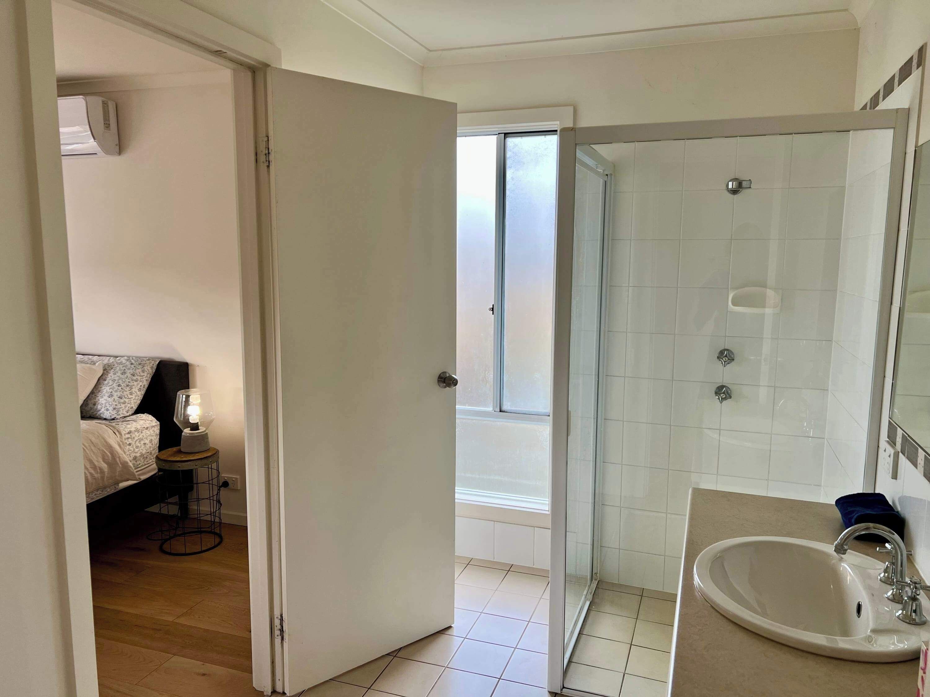 Une salle de bain avec une douche, un lavabo et un lit dans la pièce adjacente.