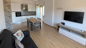 A modern living room with a black sofa, a flat-screen TV, and a wooden dining table. - Fully Renovated Accomodation (Fiumicino)