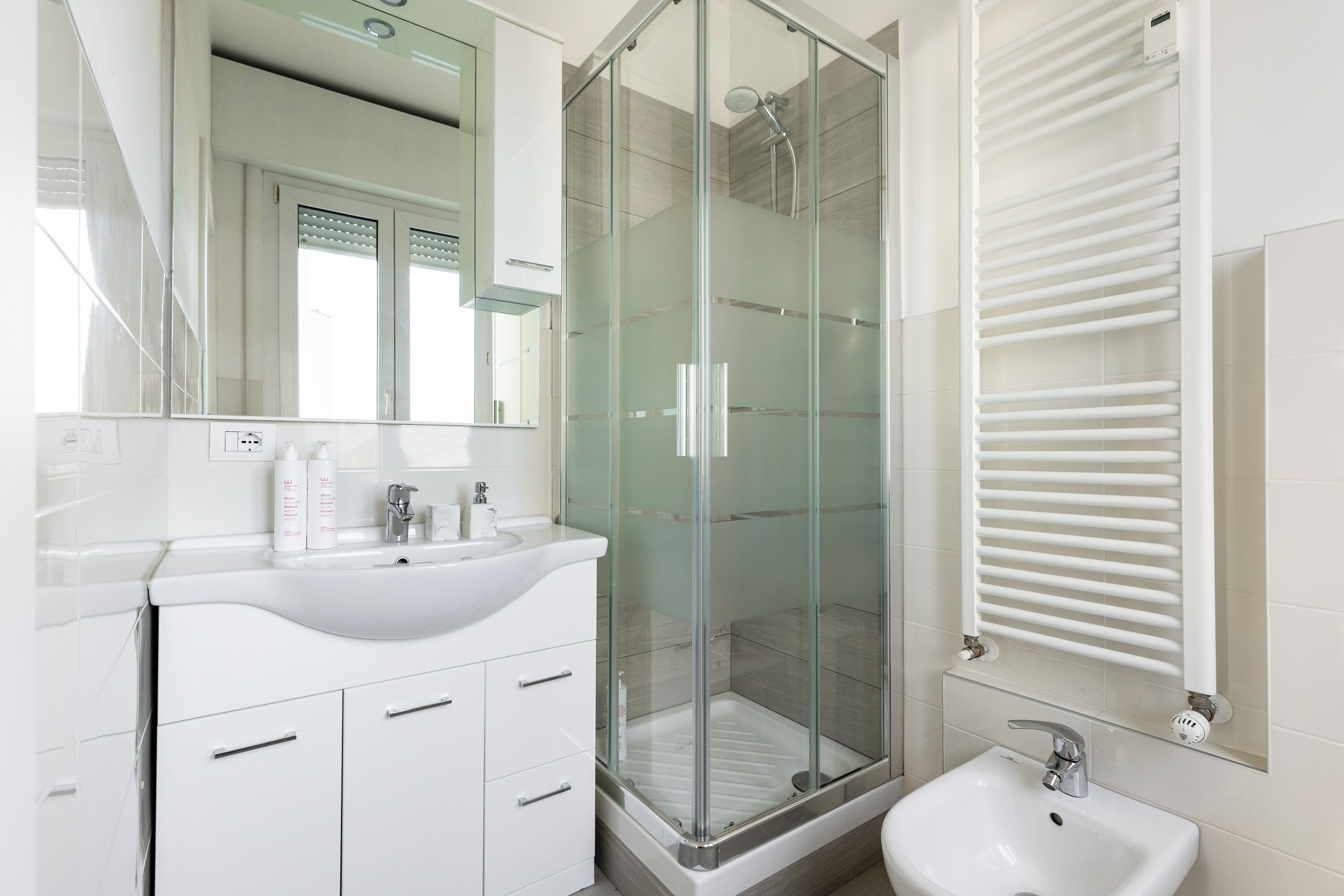 Ein modernes Badezimmer mit einer gläsernen Dusche, einem weißen Waschbecken und einem Spiegel über der Waschtischablage.