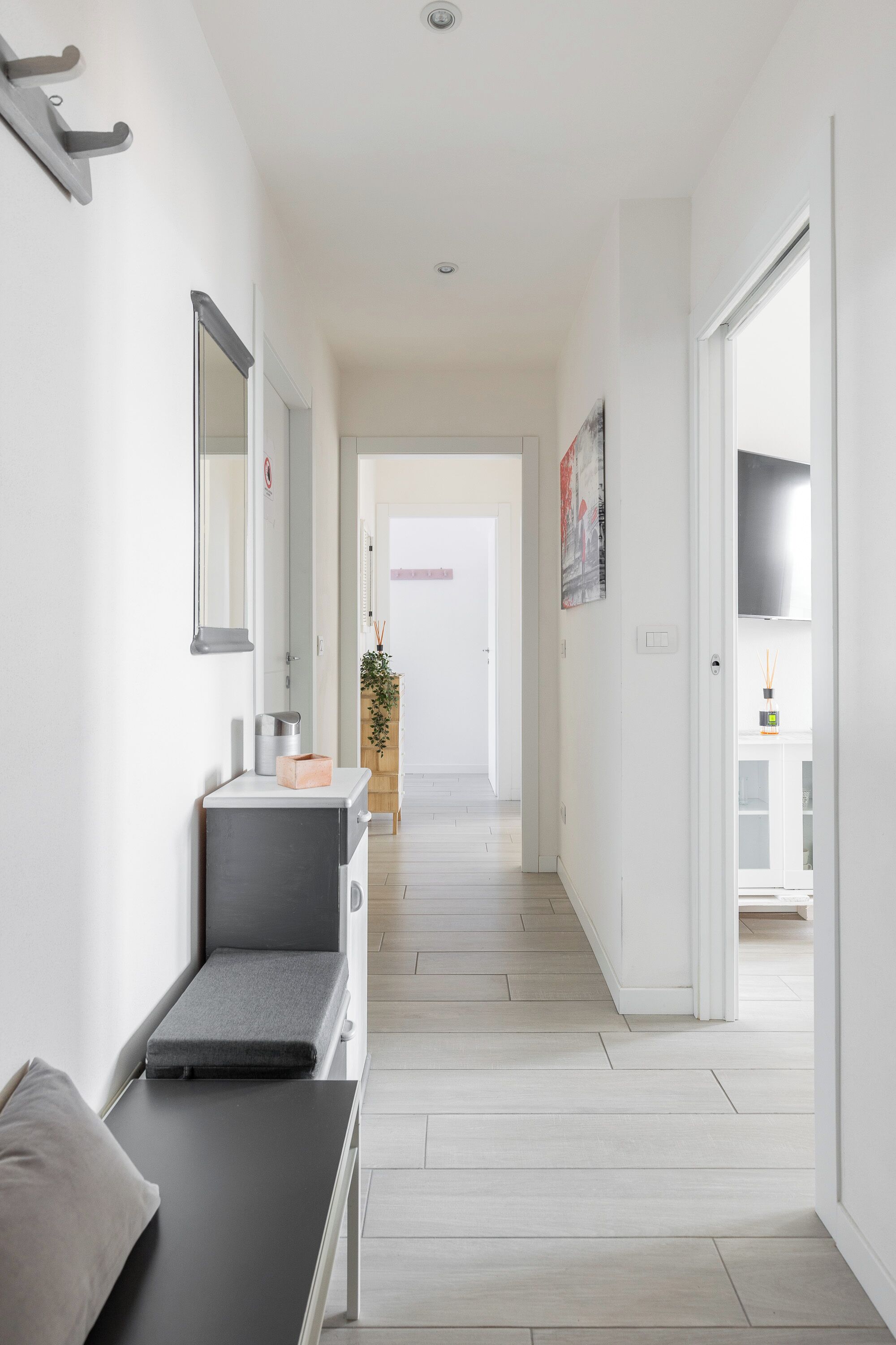 A hallway with a bench, a mirror, a small plant, and a door leading to another room.