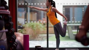 Une personne qui s’étire dans une salle de sport, avec des appareils d’exercice et une vue sur l’extérieur par la fenêtre.