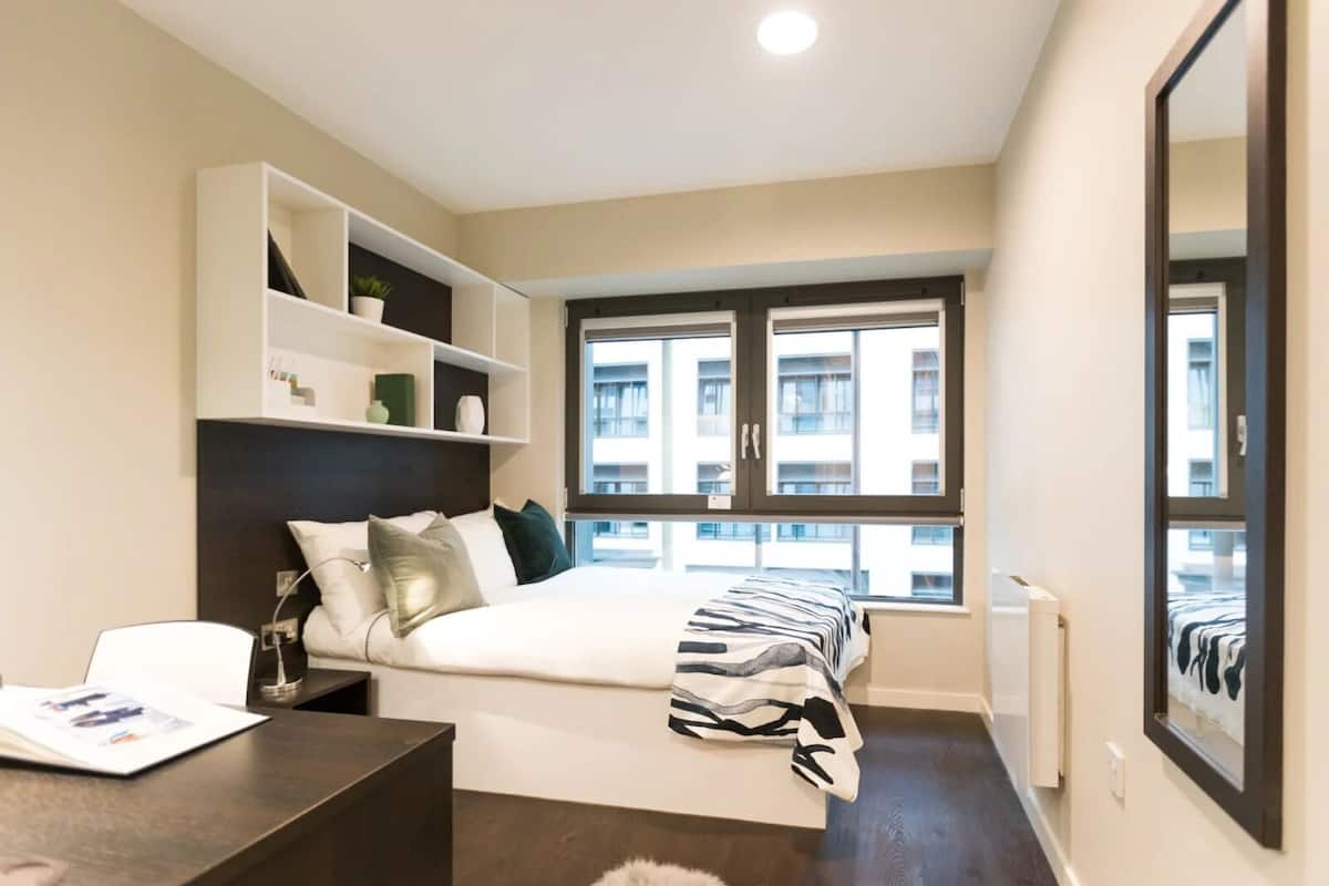 A modern bedroom with a bed, a desk, and a window with a city view.