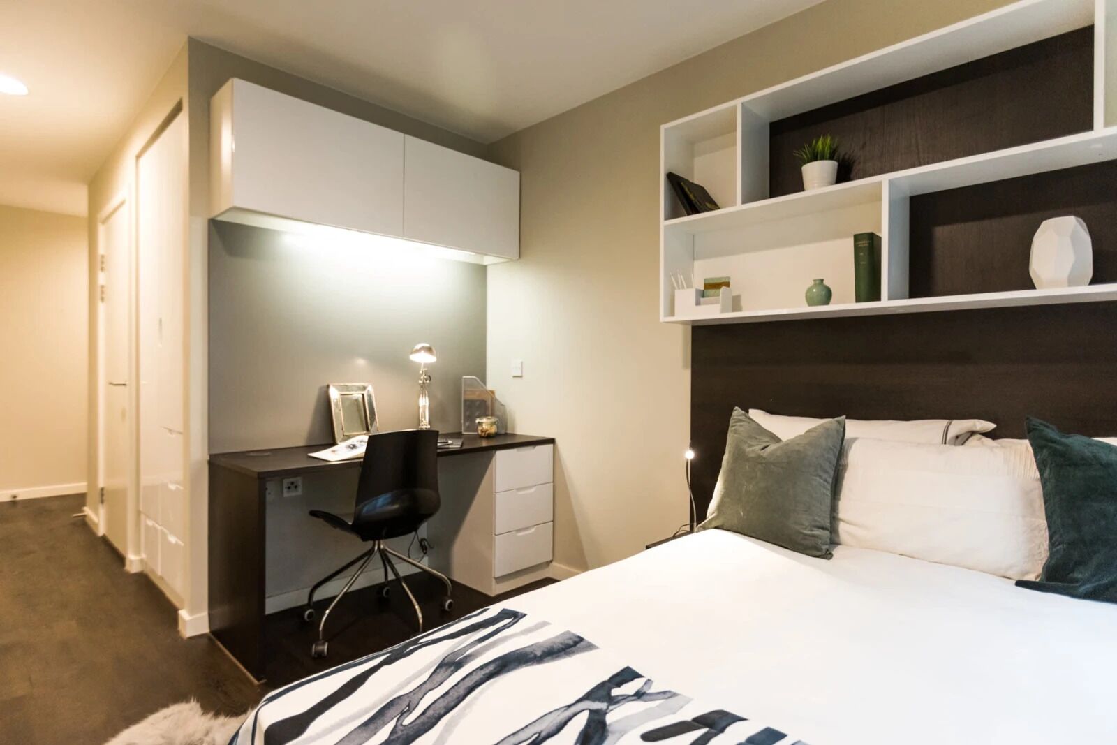 A bedroom with a bed, desk, chair, and shelving unit.