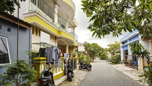 A narrow street with residential buildings, a motorcycle parked on the side, and a clothesline with hanging garments. - Hotel O Manisee 1 Homestay Syariah (Batam)