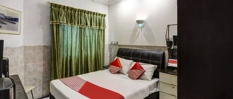 Habitación de hotel con cama, mesita de noche, espejo, ventana con cortinas y lámpara de pared.