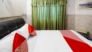 A hotel room with a bed, pillows, a headboard, a window with blinds, a green curtain, and a wall-mounted picture. - Hotel O Manisee 1 Homestay Syariah (Batam)