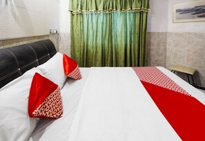 A hotel room with a bed, pillows, a headboard, a window with blinds, a green curtain, and a wall-mounted picture. - Hotel O Manisee 1 Homestay Syariah (Batam)