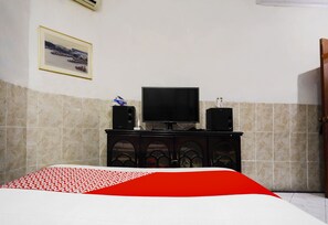 Un dormitorio con una cama, un televisor sobre un mueble y un cuadro en la pared.