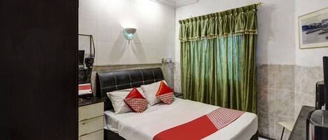 A hotel room with a bed, a bedside table, a mirror, a window with curtains, and a wall-mounted air conditioner.