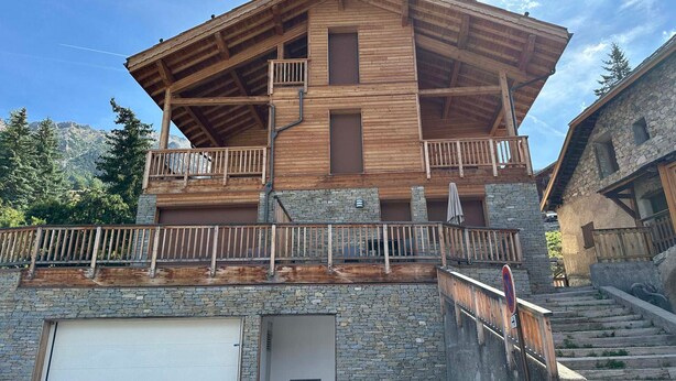 A multi-story wooden building with balconies, a garage, and stone walls. - Apartment Vars, 2 bedrooms, 7 persons (Vars)