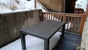 A wooden table on a snow-covered patio with a concrete wall and a wooden railing. - Apartment Vars, 2 bedrooms, 7 persons (Vars)