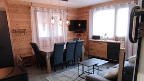 A cozy cabin-style room with a wooden interior, a dining area with blue chairs, a sofa, a TV, and a small kitchen area. - Apartment Vars, 2 bedrooms, 7 persons (Vars)
