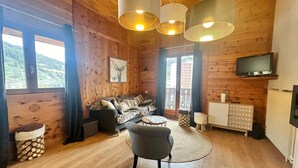 A cozy cabin interior with a wooden floor, a sofa, a chair, a television, and a fireplace.