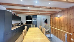 A modern kitchen with a wooden dining table and chairs, built-in appliances, and a staircase with a wooden railing.