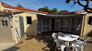 Eine überdachte Terrasse mit Tisch und Stühlen, ein Metallgitter und ein Gebäude mit einem Ziegeldach und Fenstern.