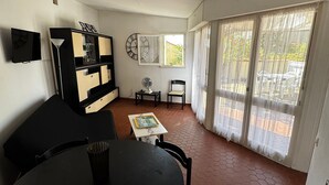 Ein Wohnzimmer mit Sofa, Tisch, Ventilator, einer Uhr und Blick durch ein Fenster.