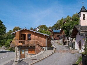 A wooden chalet with a balcony, stone walls, and a sign indicating a nearby ski lift.