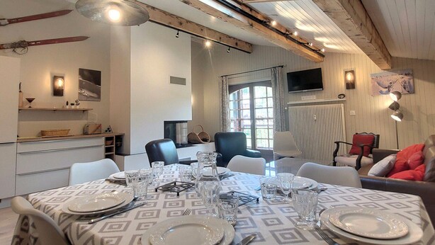 A dining area with a table set for four, a television mounted on the wall, and a window providing natural light.