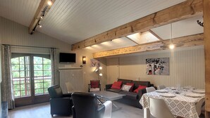 A room with a sofa, chairs, a table set for dining, a TV, and a window with curtains.