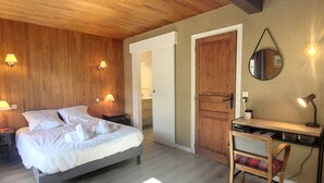 A bedroom with a bed, bedside lamps, a desk with a chair, and a mirror on the wall.