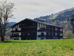 A traditional chalet-style building with multiple balconies, set against a backdrop of a mountainous landscape. - Renovated penthouse for 6 with balcony and fireplace (Les Gets)