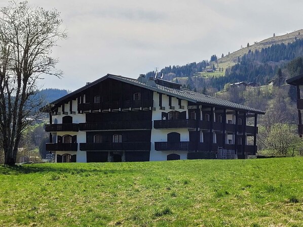 A traditional chalet with a balcony, set against a mountainous backdrop.