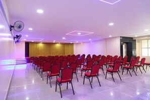 A conference room with rows of red chairs, a stage with a golden curtain, and ceiling lights. - Shri Valli Resdiency (Chennai)