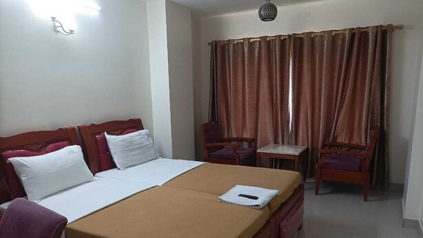 A hotel room with a bed, a desk, two chairs, a table, and a curtain. - Shri Valli Resdiency (Chennai)