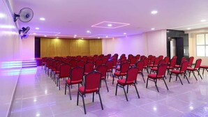 A conference room with rows of red chairs, a stage with a golden curtain, and ceiling lights. - Shri Valli Resdiency (Chennai)