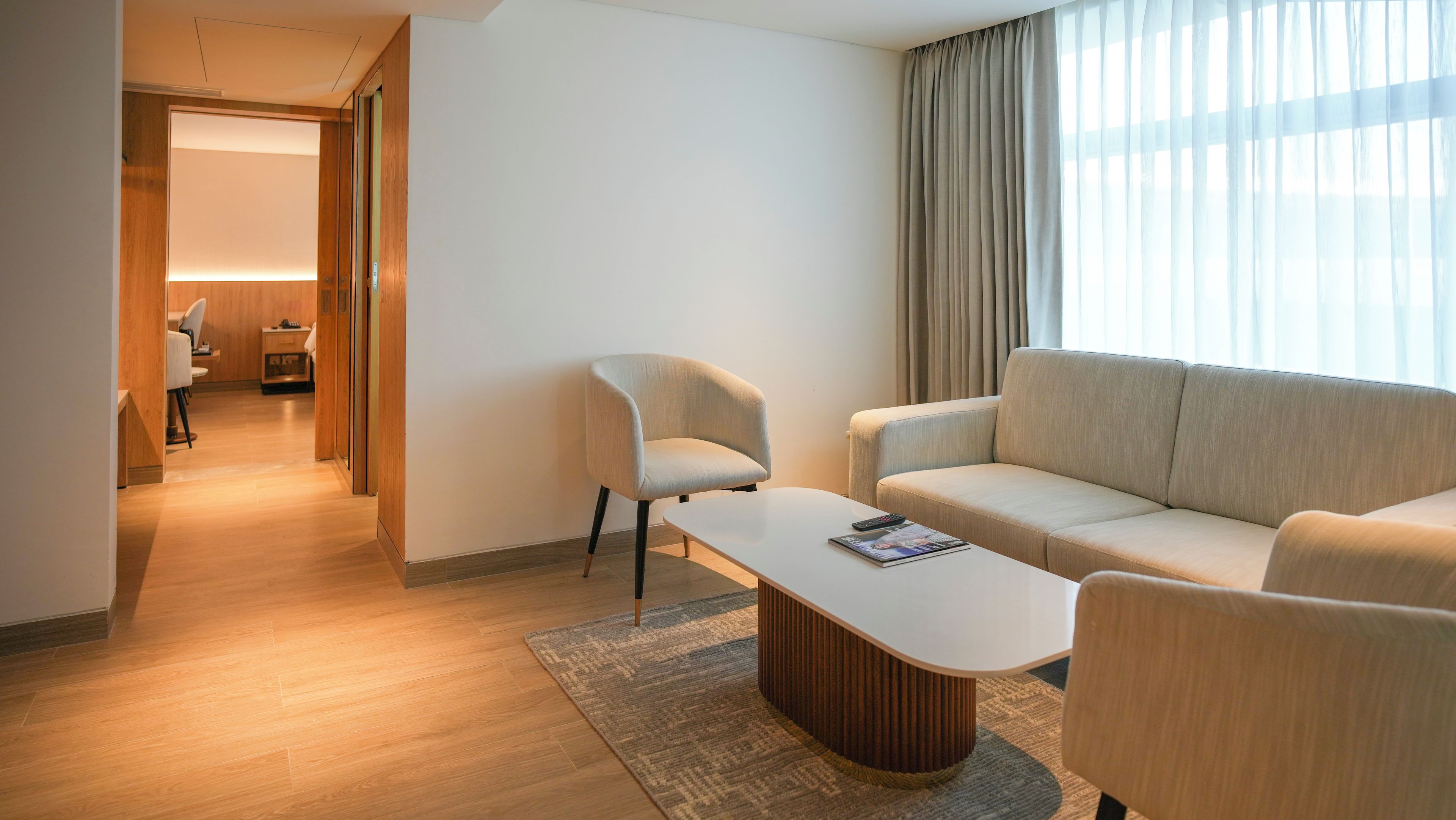 Quarto de hotel moderno com sofá, poltrona e mesa pequena.