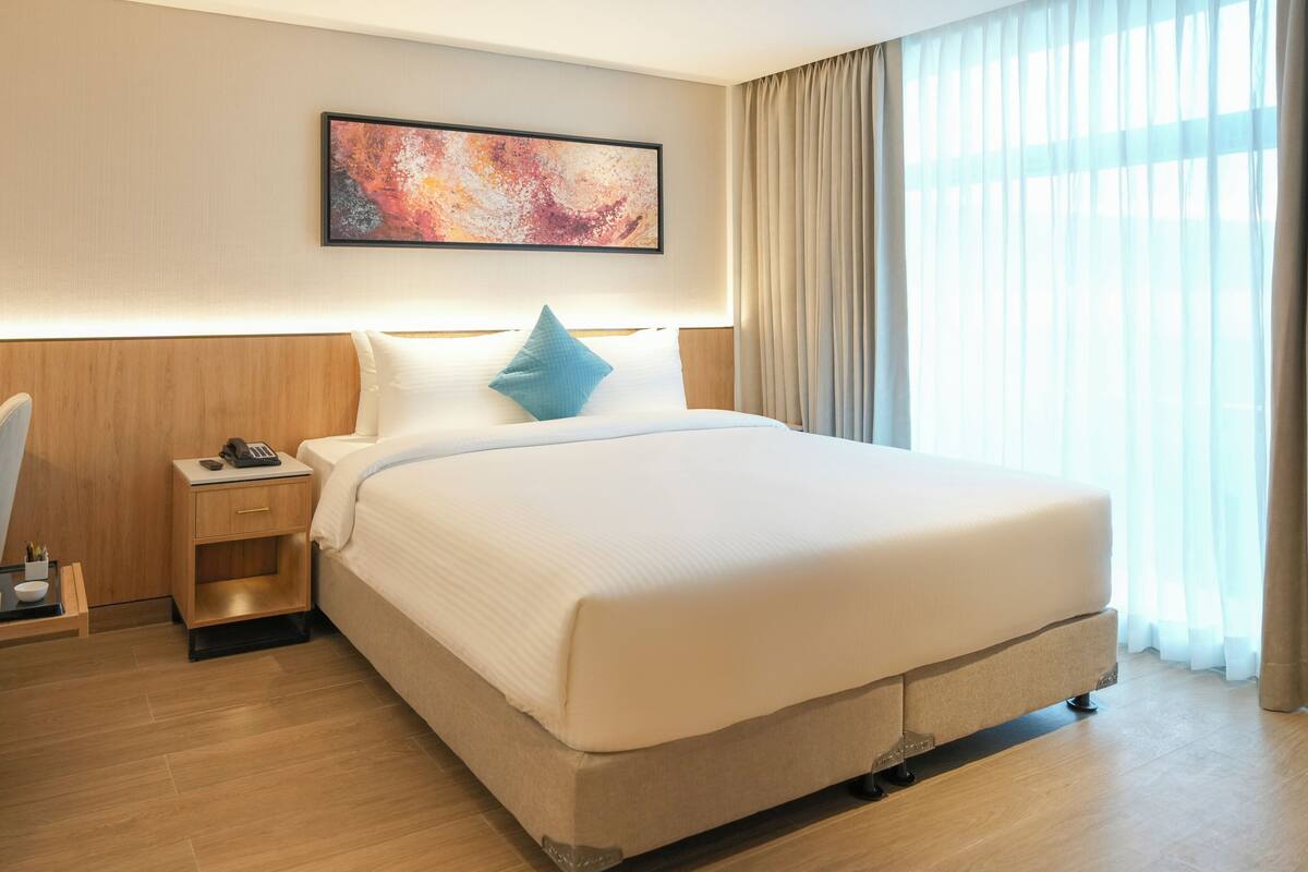A hotel room with a large bed, a desk with a phone, a small nightstand, and a painting on the wall.