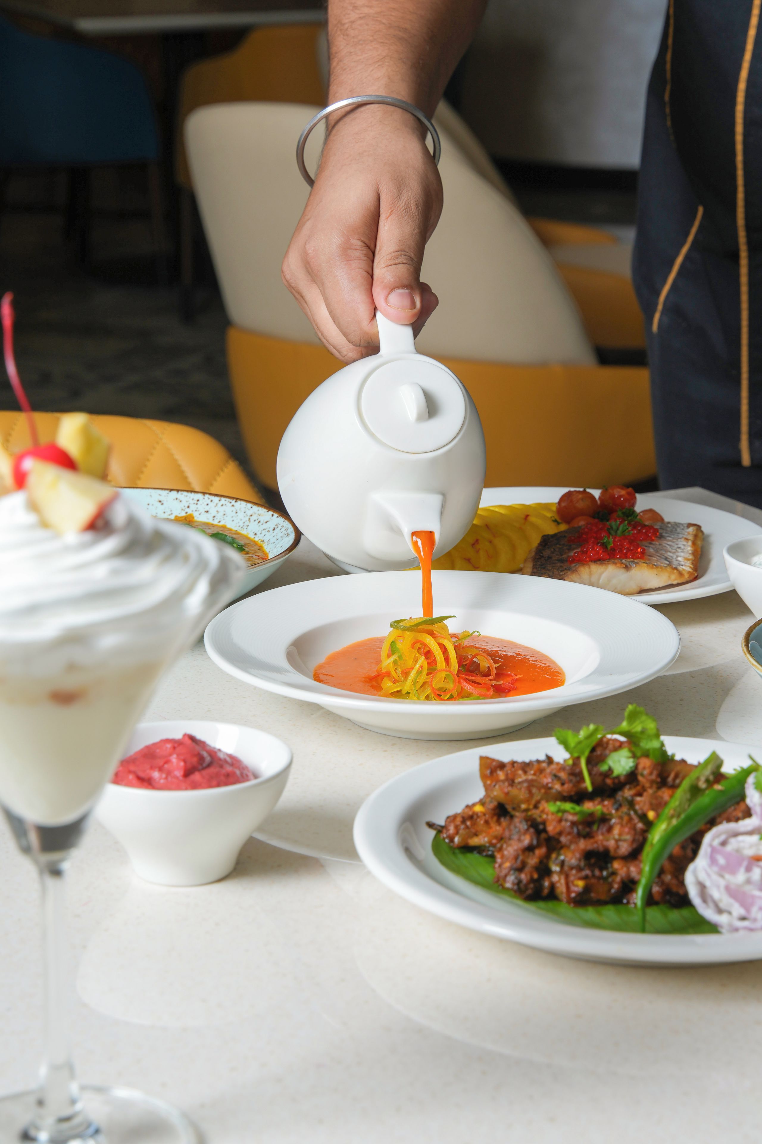 A dining table with various dishes, including a soup with vegetables, a fish dish with red sauce, and a dessert with whipped cream.