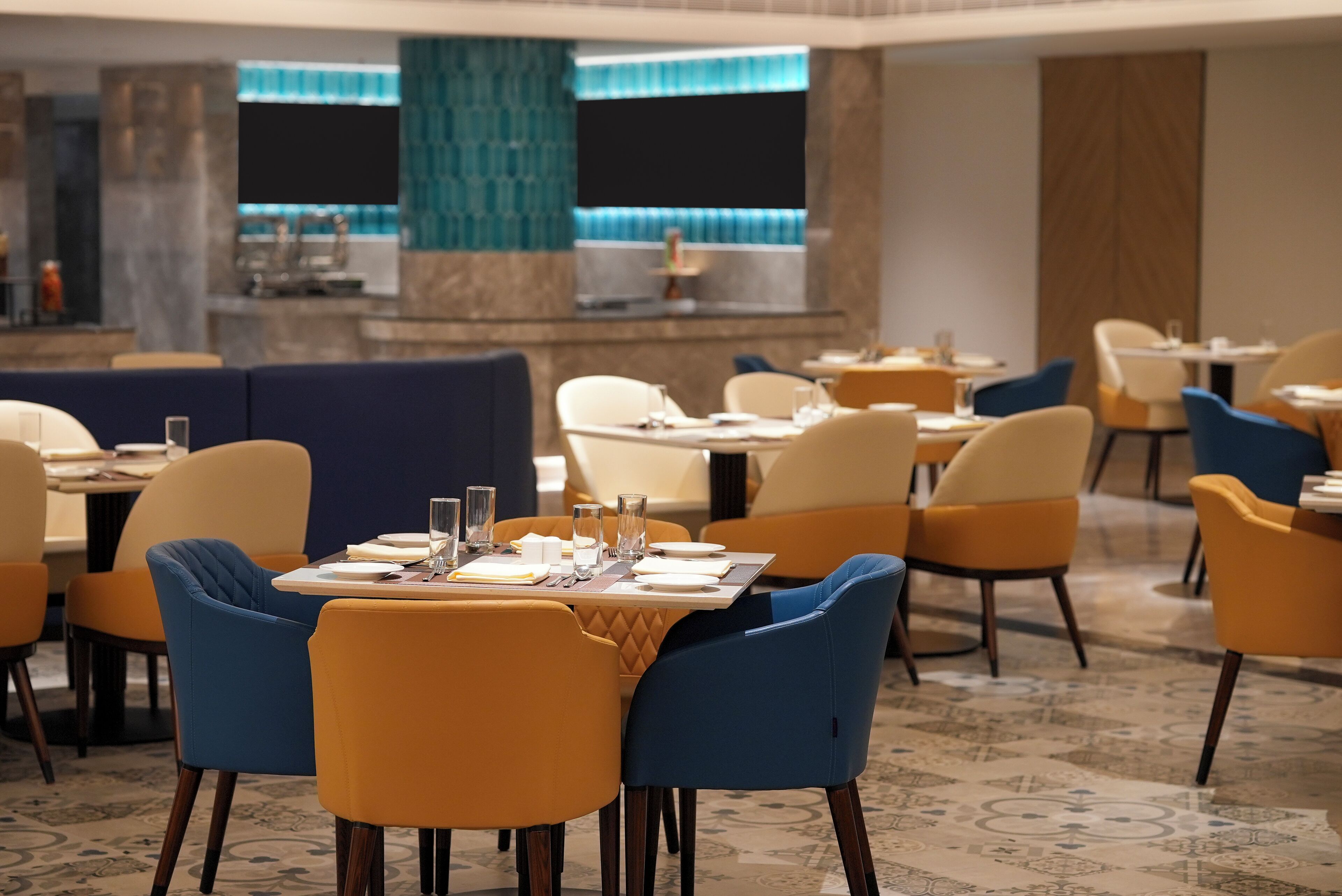 A modern dining area with tables set for four, blue and yellow chairs, and a patterned carpet.