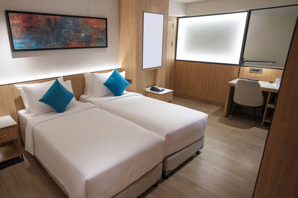 A hotel room with two beds, a desk, a chair, a large mirror, and a painting on the wall.