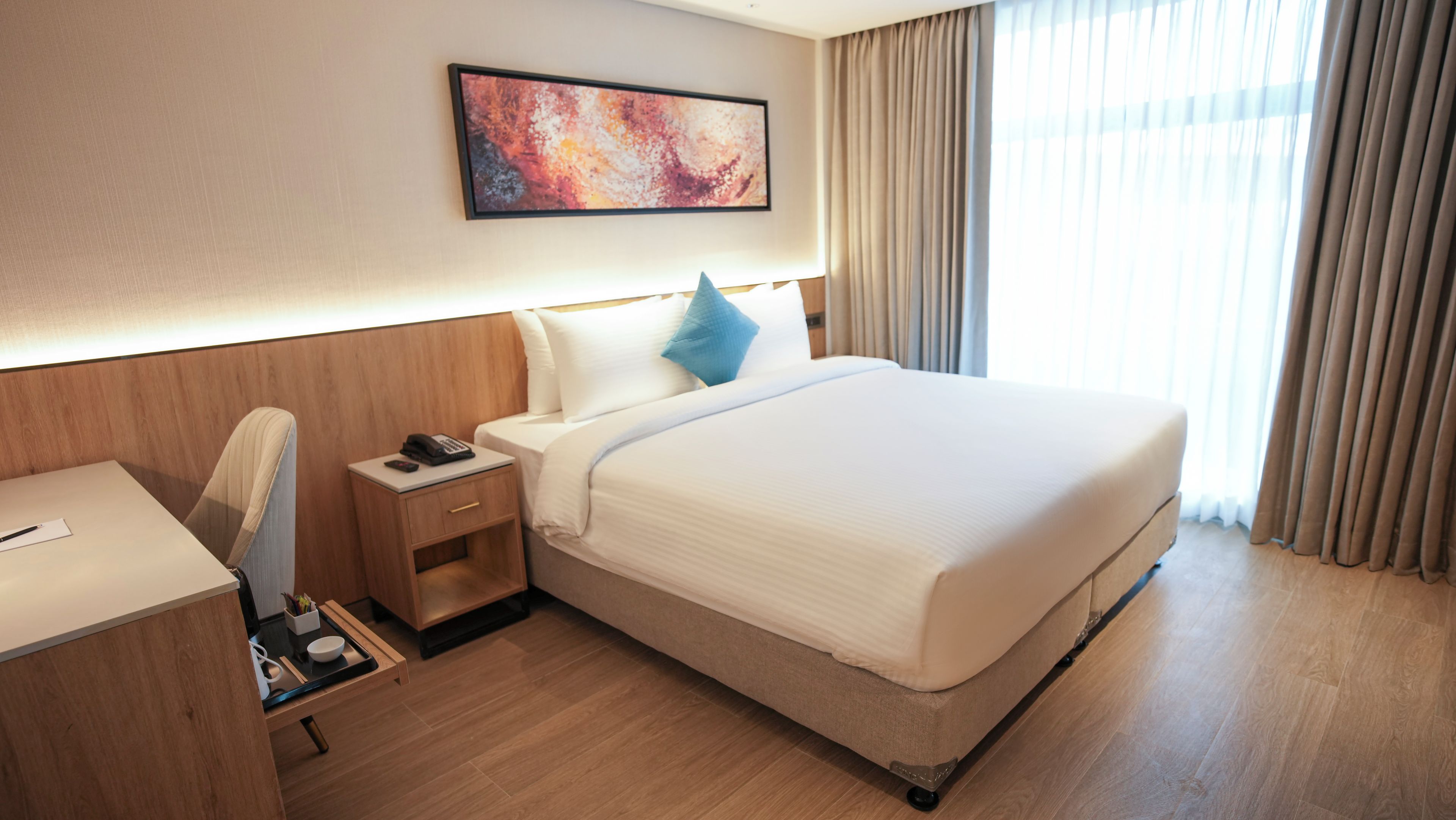 A hotel room with a bed, bedside table, chair, and a painting on the wall.