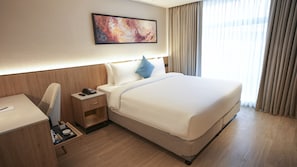 A hotel room with a large bed, a desk, a chair, a nightstand with a phone, and a painting on the wall. - Transit by Encalm - Nap and Shower (Hyderabad)
