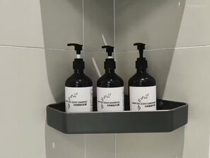 Trois flacons de produits parfumés au thé blanc sont posés sur une étagère grise dans une salle de bain.