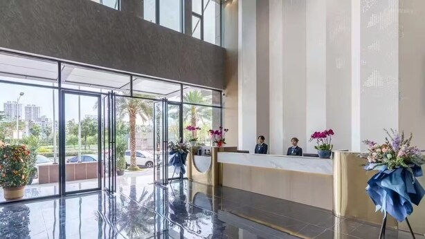 A modern hotel lobby with a glass reception desk, large windows, and potted plants. - Home Inn Wanxin Ruibo Hotel  (Beihai)