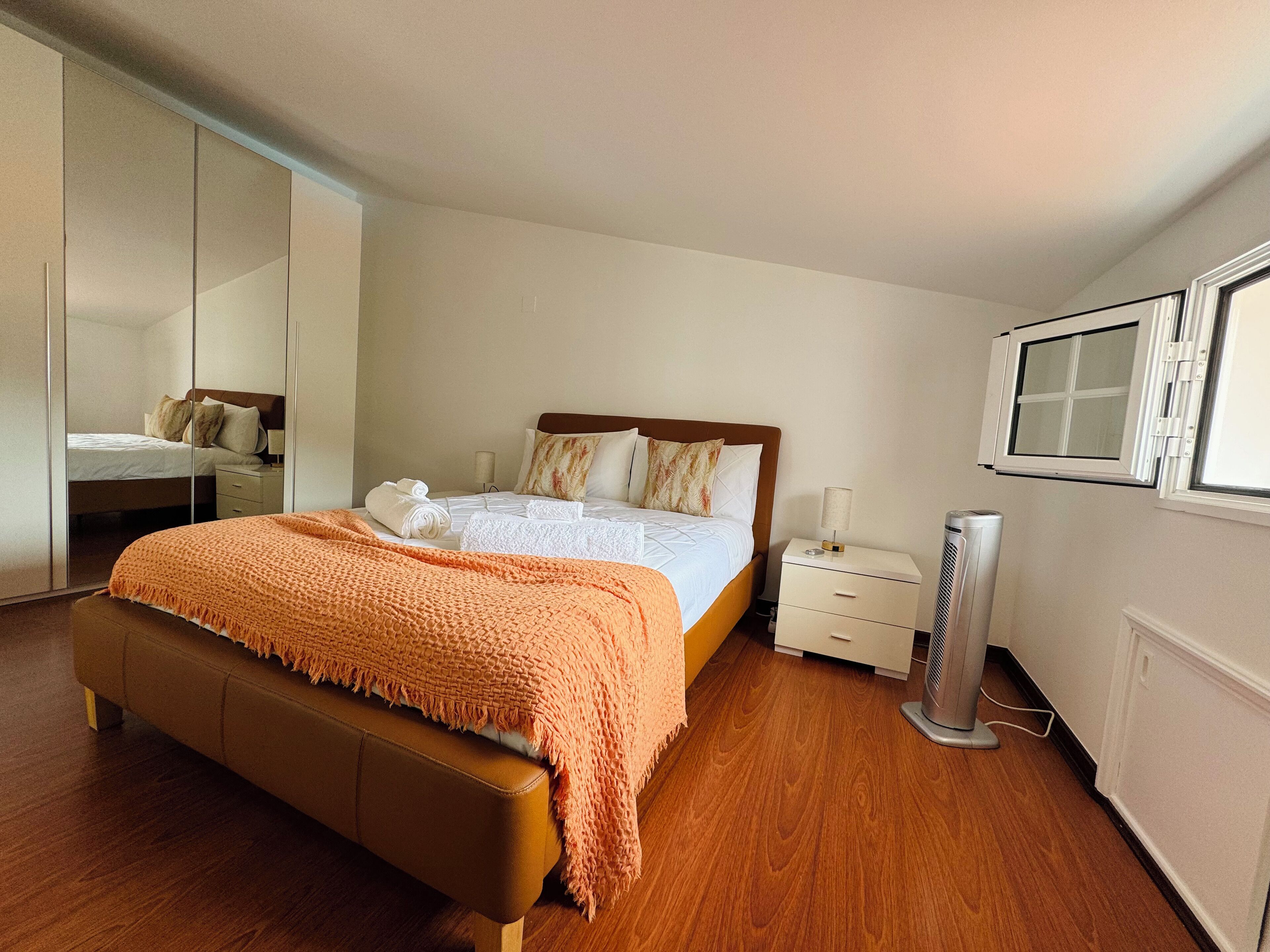 A bedroom with a bed, a bedside table, a nightstand, a mirror, and a window.