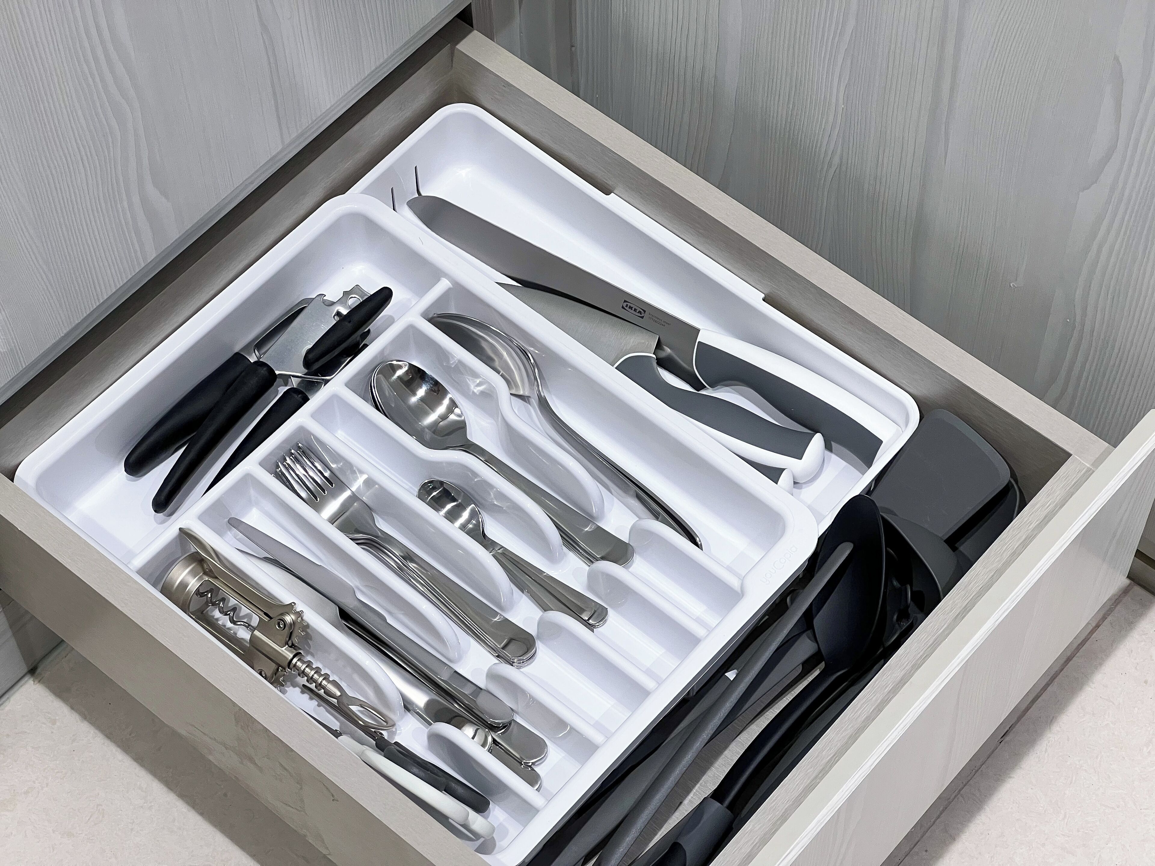 A drawer containing various kitchen utensils including knives, spoons, and a corkscrew.