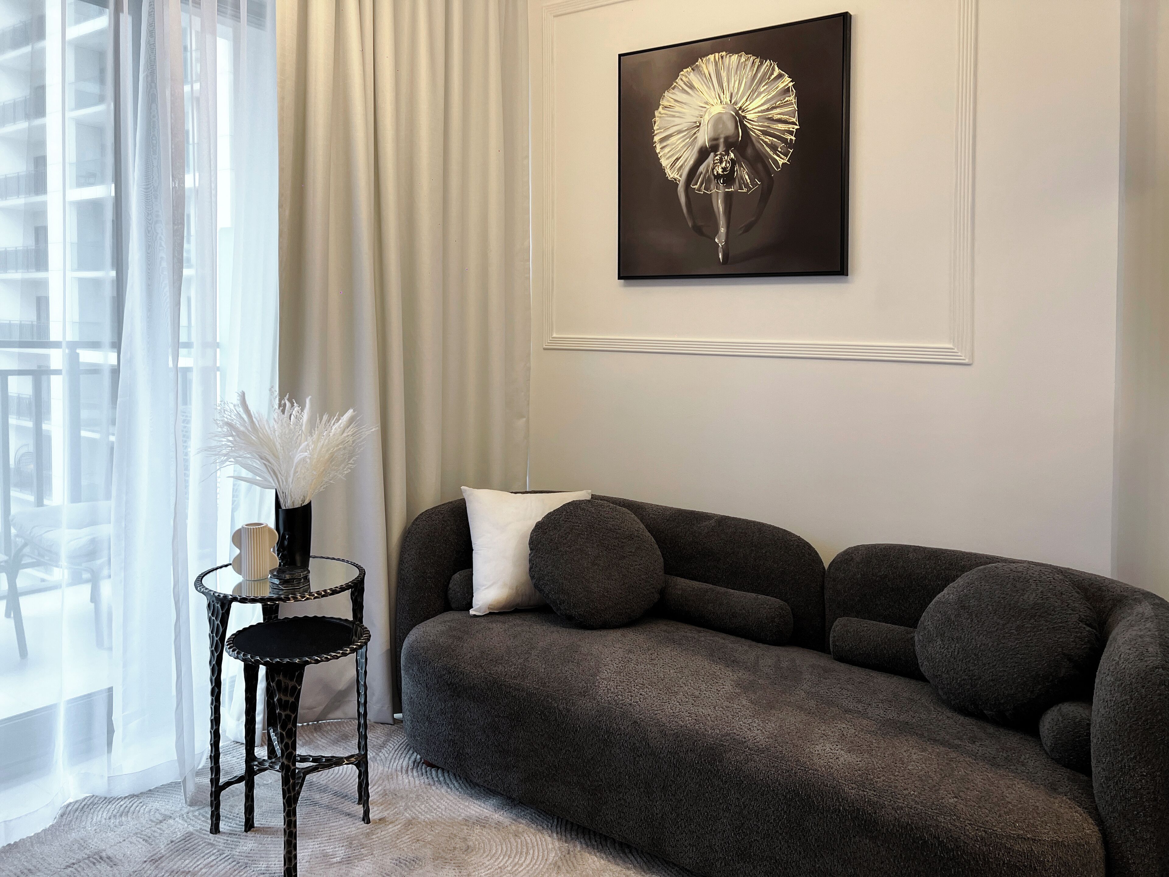 A modern living room with a dark grey sofa, a small side table with a vase of white flowers, and a large abstract gold artwork on the wall.