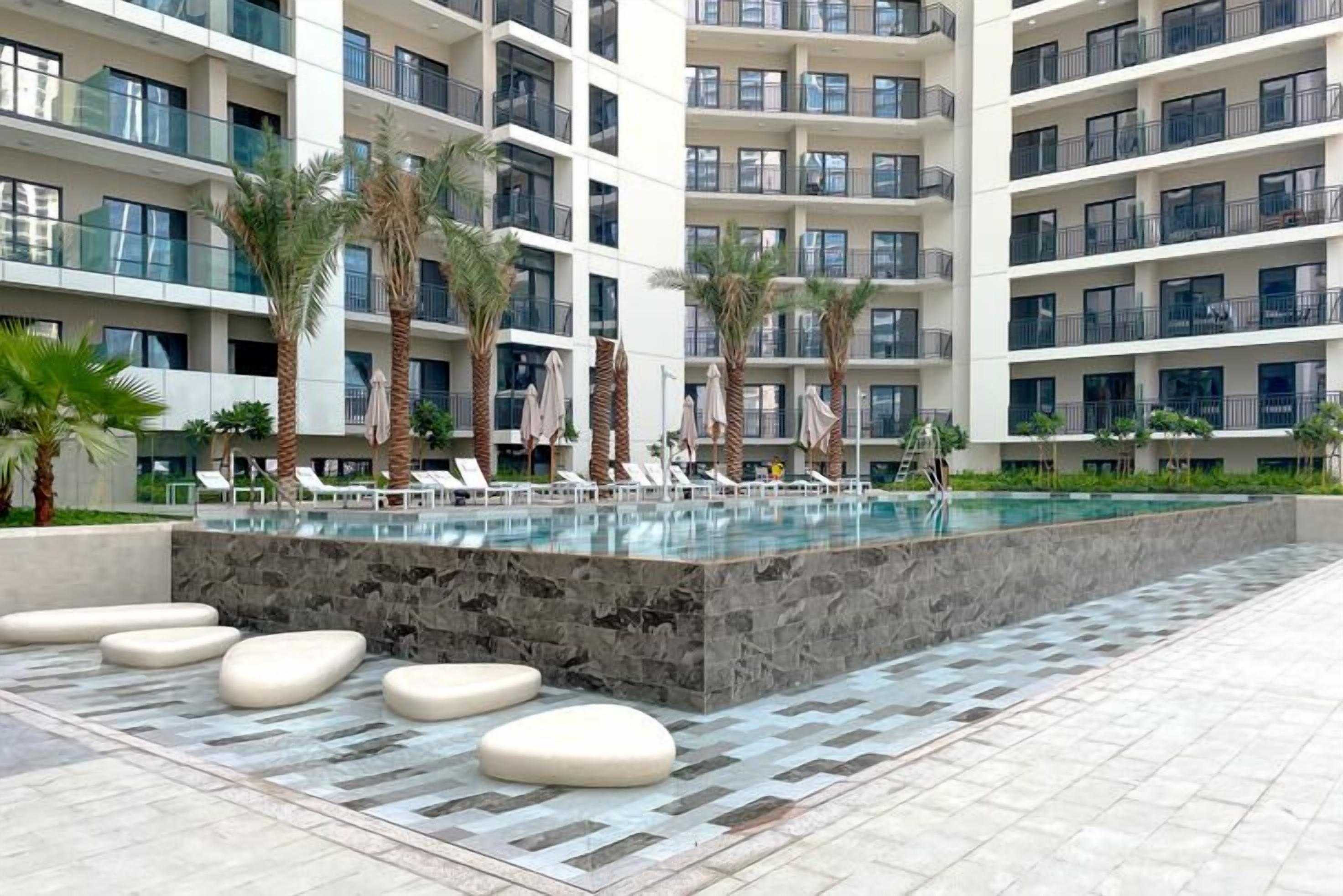 A modern hotel with a large pool, palm trees, and lounge chairs.