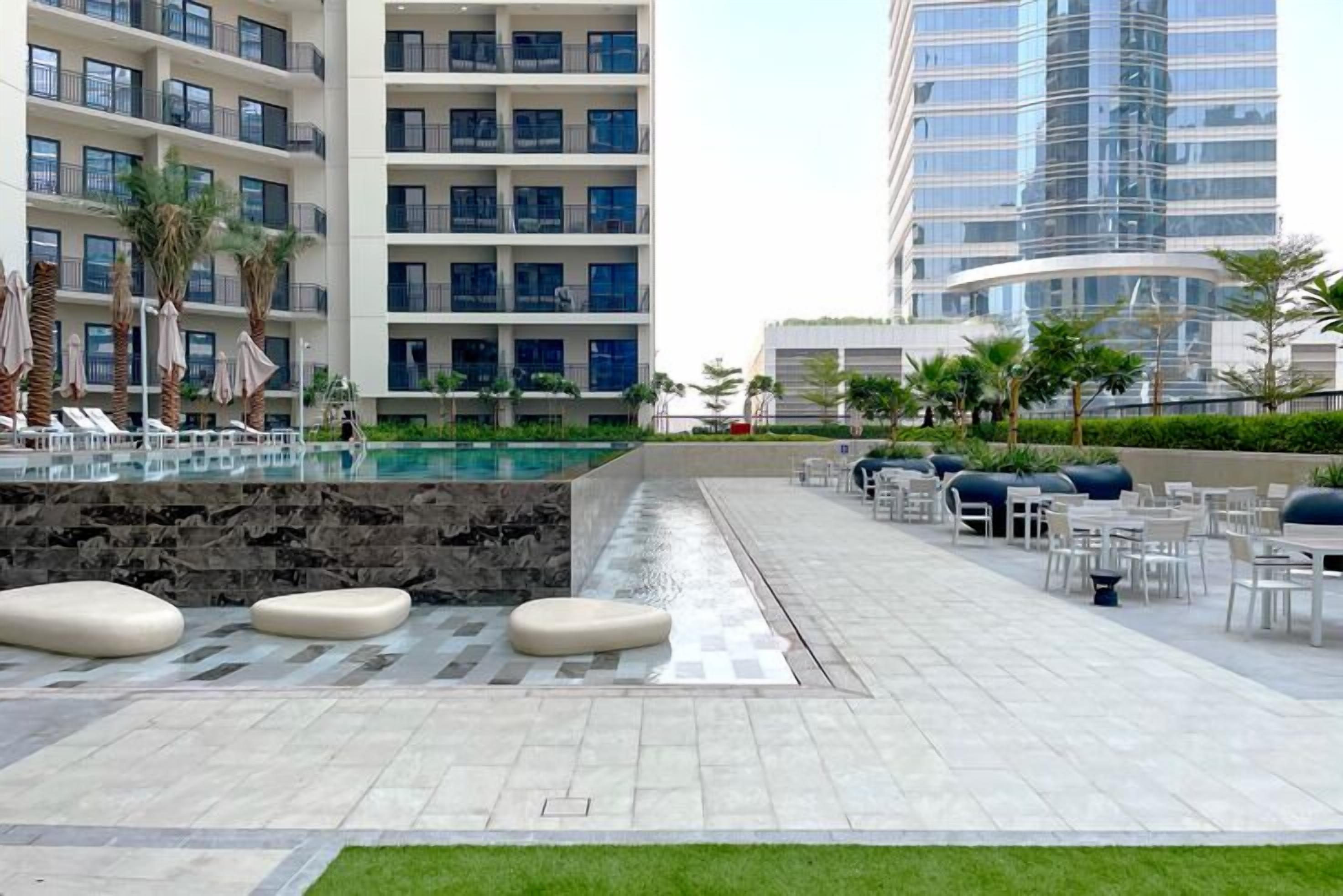 A hotel courtyard with a swimming pool, outdoor seating, and modern buildings in the background.