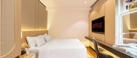 A modern hotel room with a neatly made bed, a desk with a chair, a wall-mounted TV, and a clock.