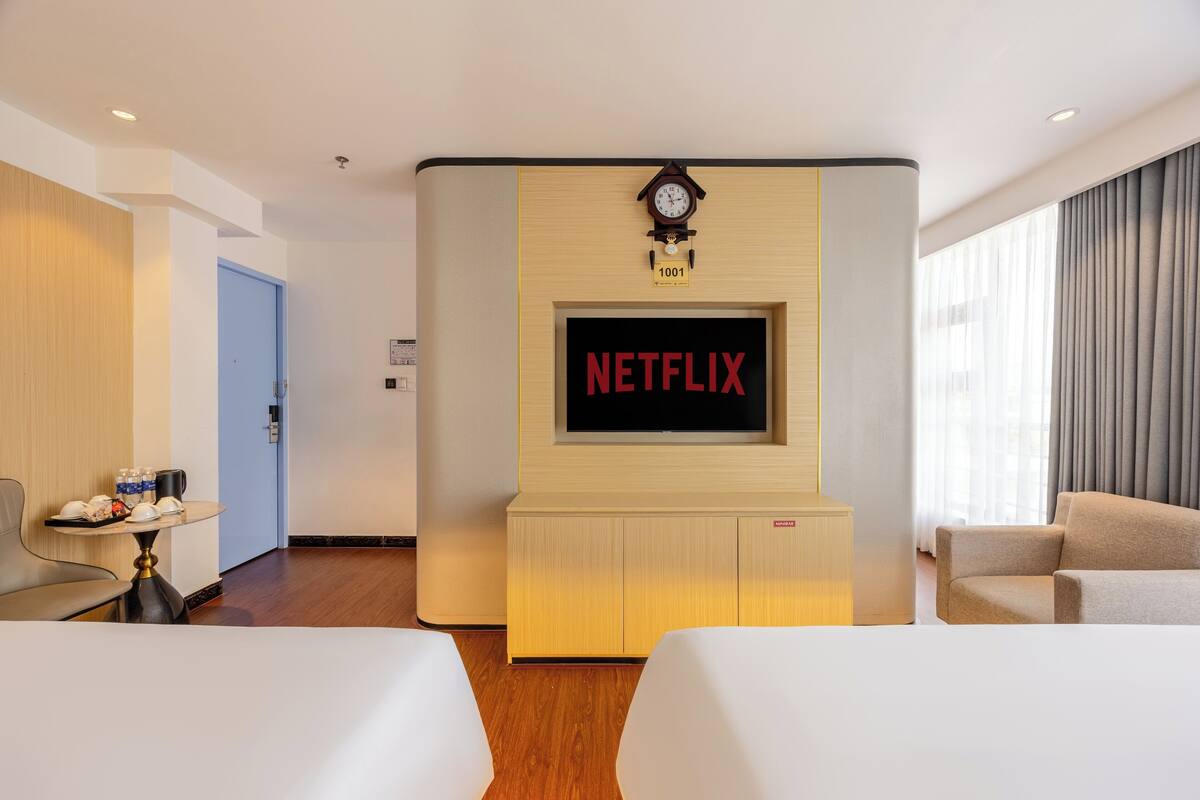 Habitación de hotel con un televisor de pantalla plana grande montado en la pared, un reloj encima y una puerta a la izquierda.