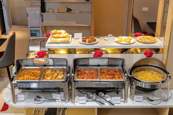 Een buffet met diverse gerechtjes, zoals belegde broodjes, gebak en een grote pan rijst.
